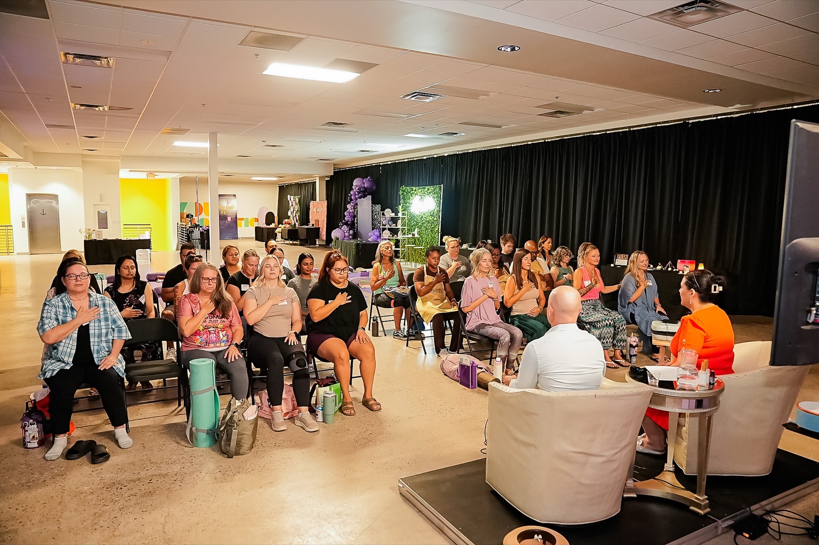 Both hosts guide a breathwork moment, hands on hearts across the room